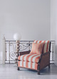 An upholstered cane chair featuring Nomad striped woven fabric in Coral paired with Boundary from the And Objects Collection, set in an elegant minimalist hallway. The blend of classic nostalgia and clean modern lines, combined with the contemporary coral hue, creates a timeless yet fresh aesthetic that balances heritage and modern design.